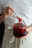 The man holds a jar of homemade strawberry jam in his hands