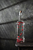 A bottle of homemade liquor with berries on a wooden stool