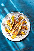 Fried fish fillets on an orange and onion salad with fennel and edible flower petals