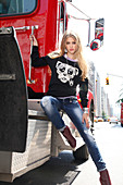 Young blonde woman wearing jeans and jumper with dog motif sitting on truck
