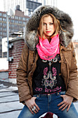 Junge blonde Frau in Winterjacke mit Kapuze, Motivpulli und Jeans