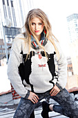 Young blonde woman wearing knitted jumper with animal motif and grey trousers