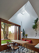Dining table below light shaft and next to large window overlooking garden