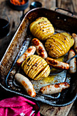 One pan dish of Hasselback potatoes with harissa butter and grilled pork sausages