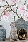 Rabbit figurine and small nest under flowering magnolia branches in vase