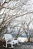 Weiß lackierte Holzbank unter Baum mit Laternen im winterlichen Garten