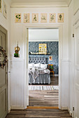 View through open door into bedroom with double bed and blue-patterned wallpaper