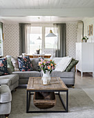 Sofas, coffee table with antique wooden trough and patterned wallpaper in bright living room