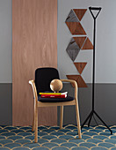 Chair in front of wooden panel next to triangles of wooden veneer on grey wall