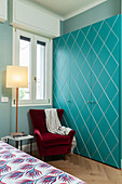 Turquoise fitted wardrobe, red velvet armchair and standard lamp in bedroom