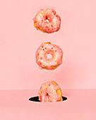 Bunch of tasty doughnuts with sweet icing falling into round hole on pink background