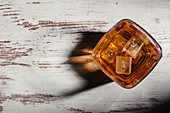 Glass of scotch in rays on aged rustic table in darkness