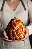 Crop housewife in apron holding appetizing tasty homemade braid bread with sprinkles