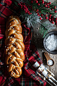 Traditional braided bread and knife placed on checkered Christmas tablecloth with decorative objects