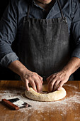 Making hole in dough while forming artisan round bread loaf at wooden table