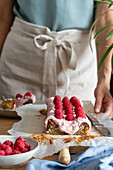 Crop anonymous female with appetizing homemade cake with glaze and fresh raspberries