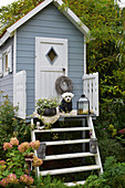Kleines Gartenhaus mit bepflanzter Schale und Hund auf Lammfell, Kranz am Türknauf, Laterne