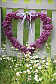 Heart wreath made of lilac blossoms for Mother's Day hung on the fence, with a flower meadow with daisies