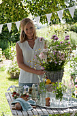 Frau bringt Strauß aus Rosen und Sommerblumen zum gedeckten Tisch