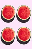 Four watermelon halves on a pink background