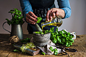 Man preparing herbal pesto with basil and olive oil in a mortar on the table