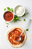 Raw pizza base being spread with tomato sauce