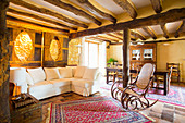 Sofagarnitur und Schaukelstuhl in offenem Wohnraum mit rustikaler Holzbalkendecke