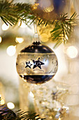 Silver-and-blue Christmas bauble hung from branch in front of sparkling lights