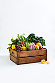 Fresh fruit and vegetables in a wooden crate against a white background