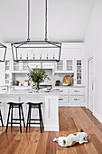 White kitchen with kitchen island, black bar stools and hanging lamp