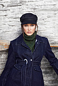 A young woman wearing a cap, a denim coat and a green turtlenneck