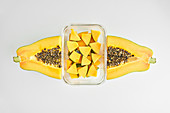 Papaya and glass container with pieces of fresh fruit placed on white background