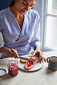 Frau streicht Beerenmarmelade auf Frühstücksbrot