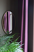 Blick über Zimmerpalme auf Wandspiegel neben lila Vorhang