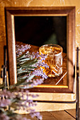 Old fashioned glass with alcohol drink placed on table with lavender flowers and reflected in mirror