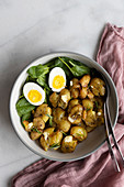 Smashed roasted potatoes in a salad bowl with baby spinach and hard boiled eggs
