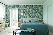 Doppelbett mit Tagesdecke und Bank im Schlafzimmer, Tapete mit Pflanzenmotiv