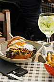 Juicy burger with fried egg and fries on table with glass of cool lime cocktail in cafe