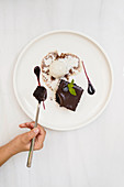 Top view of faceless person having bite of chocolate square cake with ganache and ice cream