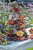 Selbstgebaute Etagere aus Holzscheiben und Stammstücken von Birke, dekoriert  mit Rosen, Äpfeln, Kastanien, Haselnüssen und Blättern vom wilden Wein