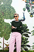 A grey-haired woman wearing a green jumper and pink trousers