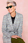 A grey-haired woman wearing a checked blazer and green trousers