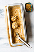 Tahini almond milk ice cream in a loaf cake tin with an ice cream scoop and sesame seeds on the side.