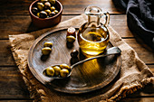 Glass jar with extra virgin oil placed on wooden plate with black and green olives