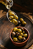 Olivenöl über Löffel in Keramikschale mit Oliven giessen