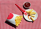 French fries packet near plate with potatoes soaked in ketchup