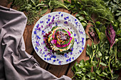 Tasty dish garnished with flower petals and placed on wooden table with various greenery