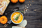 Flatlay of fresh pumpkin soup garnished with sour cream, toasted pumpkin seeds and thyme with homemade artisan bread in the background.