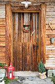 Rustic front door of wooden house decorated with lantern, conifer and wreath