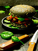 A black burger bun with Nuremberg sausages, spinach, ketchup and tomatoes